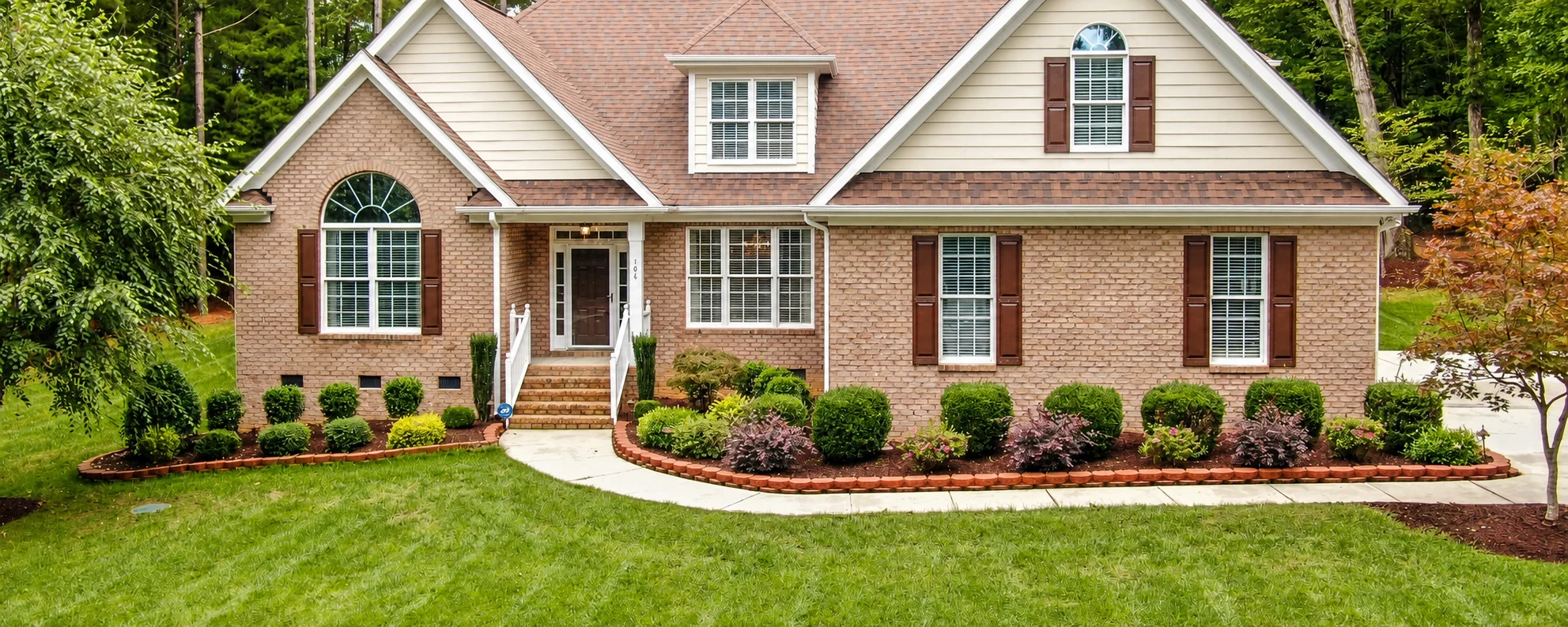 Bright green front lawn and landscaped garden in front of a brick home
